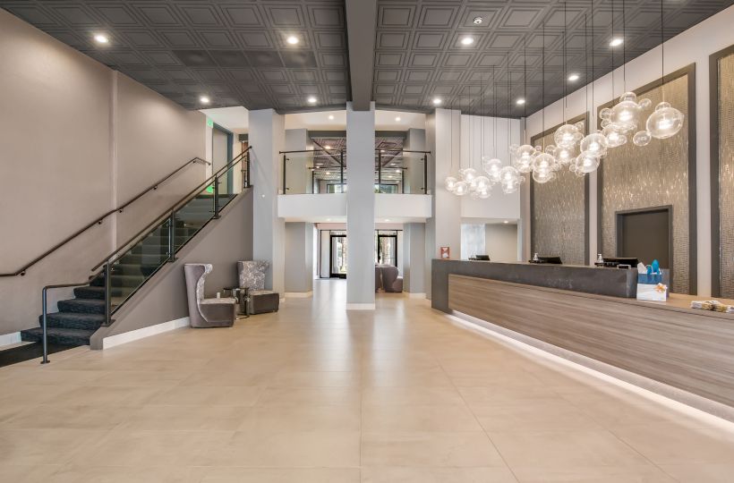 The image shows a modern hotel lobby with a staircase, a reception desk, stylish lighting fixtures, and seating areas in a spacious and elegant setting.