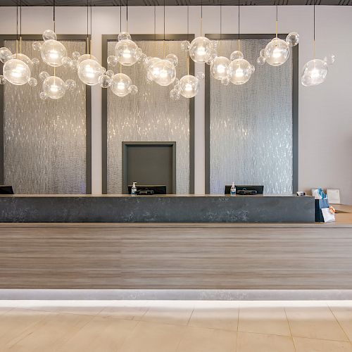 The image shows a modern reception area with a wooden desk, hanging bubble lights, a door in the middle, and some shelves with items on the right side.