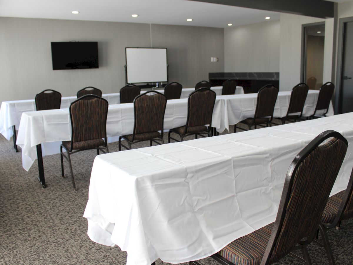 The image shows a conference room setup with rows of chairs and tables covered in white cloths, a TV, and a whiteboard at the front.