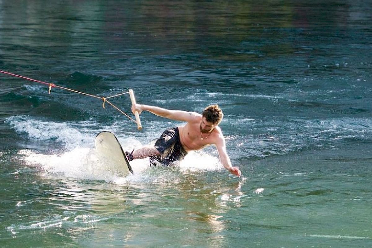 A person is wakeboarding on a body of water, holding a rope handle, and appears to be losing balance while riding over the water's surface.