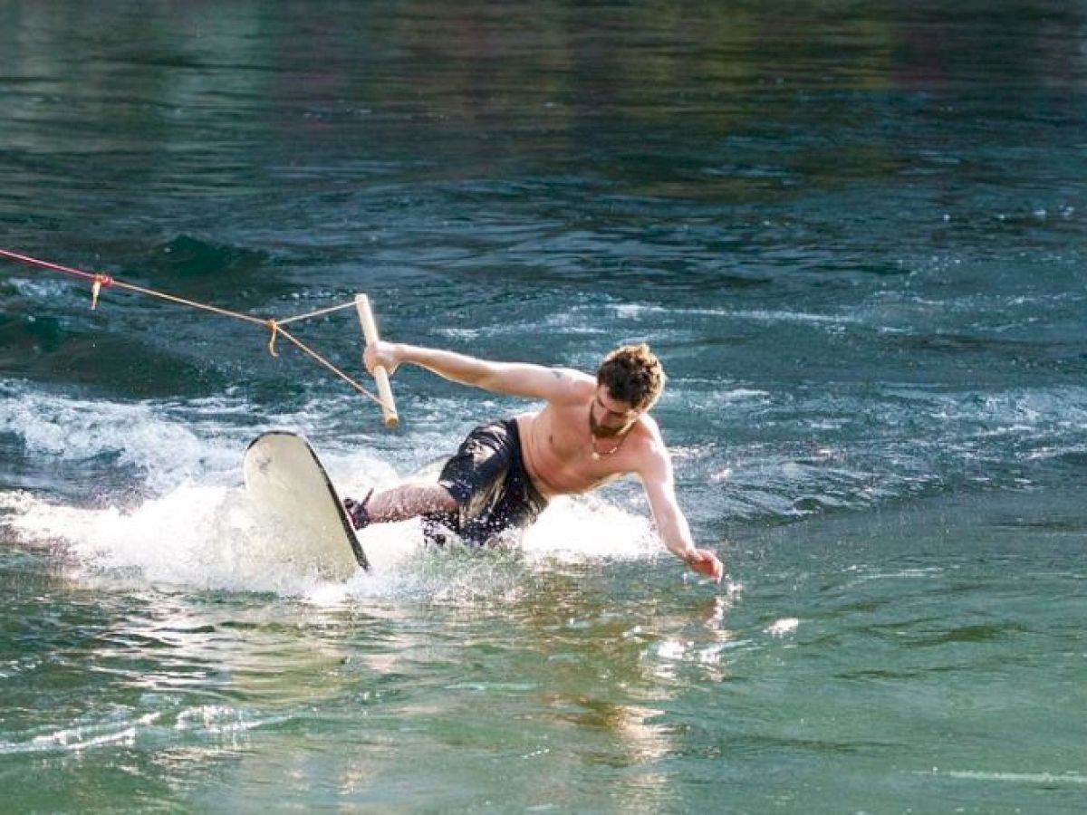 A person is wakeboarding on a body of water, holding a rope handle, and appears to be losing balance while riding over the water's surface.