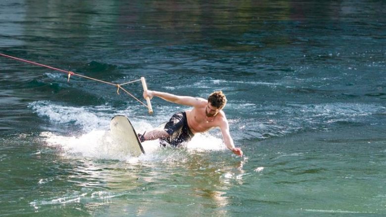 A person is wakeboarding on a body of water, holding a rope handle, and appears to be losing balance while riding over the water's surface.