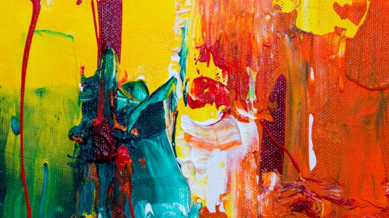 This image is a colorful abstract painting featuring vibrant hues of yellow, red, orange, green, and blue with dynamic brushstrokes and drips creating texture.