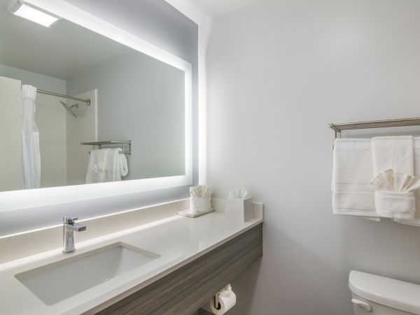A modern bathroom with a large backlit mirror, sink, and neatly arranged white towels on a rack in a minimalistic design.