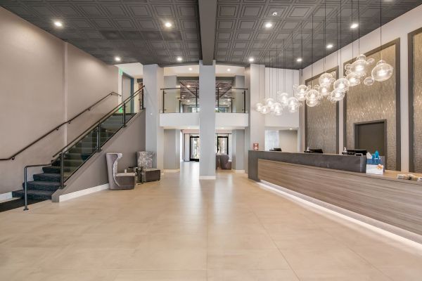 A modern hotel lobby features a reception desk, a staircase, seating areas, elegant lighting, and neutral tones.