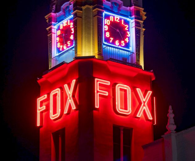 The image shows a brightly lit clock tower with red neon signs that read 