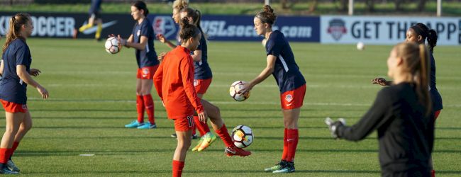 A group of female soccer players is practicing on a field during a training session, with some juggling soccer balls.