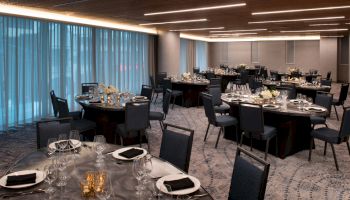 An elegant banquet hall with round tables, set with black napkins, glassware, and floral centerpieces, ready for an event.