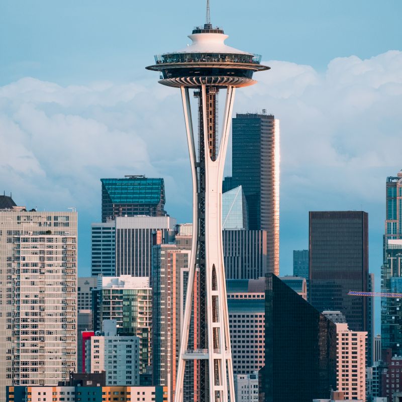 The image showcases the Seattle Space Needle with the downtown city's skyscrapers in the background, under a mostly clear sky.