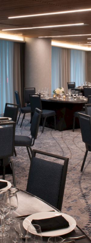 A banquet hall with round tables covered with black tablecloths, set with glassware, cutlery, and floral centerpieces, and chairs arranged around them.