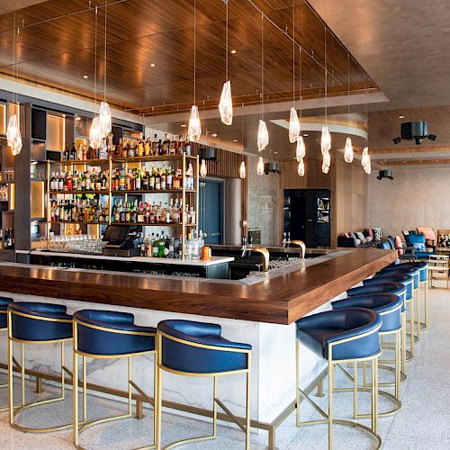 A modern bar with stylish seating, hanging lights, and a well-stocked counter. The area also features lounge seating and a sleek interior design.