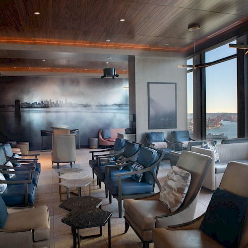 A modern lounge area with plush seating, large windows showcasing a scenic view of a waterfront and Ferris wheel in the background.